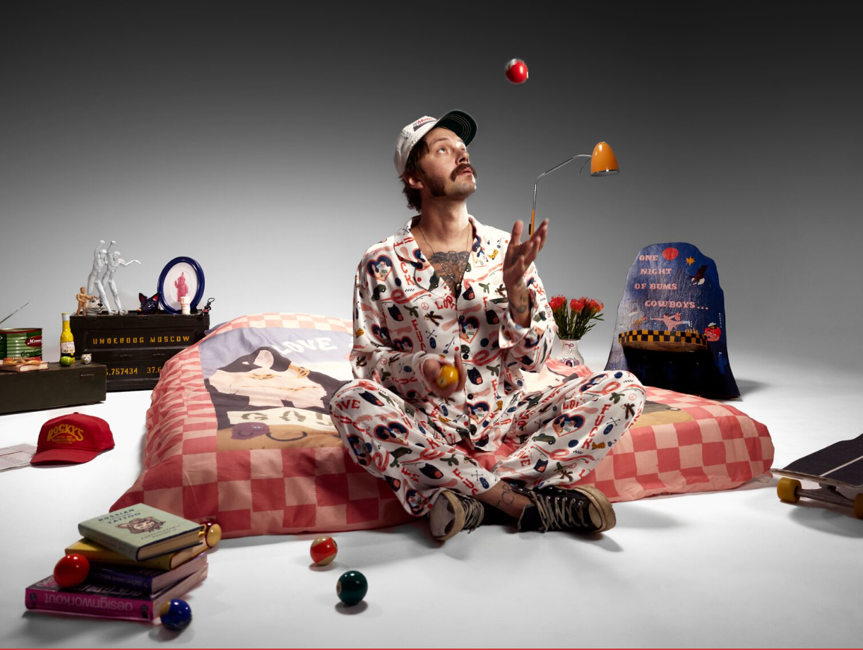 Artist juggling on a bed surrounded by illustrated textiles and art objects